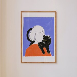 May include: Framed art print featuring a stylized illustration of a person with short white hair and an orange top, holding a black cat with yellow eyes. The background is a solid blue color.