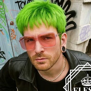 Puede incluir: La imagen muestra a una persona y un maniquí, ambos con cabello verde brillante. La persona lleva gafas teñidas de rosa, una chaqueta de cuero negra y pantalones blancos. El maniquí tiene un collar con un colgante. El logo "ELESSA" está en el centro.