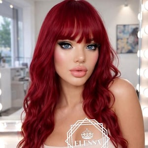May include: A long, wavy, vibrant red wig featuring straight-cut bangs. The hair has a deep crimson hue with soft, flowing waves that cascade down the shoulders. A white geometric logo with a crown icon and the text ELESSA is centered.