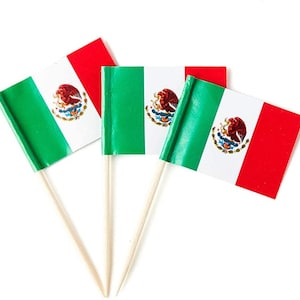 May include: Three small Mexican flags on wooden skewers. Each flag is green, white, and red with the Mexican coat of arms in the center.