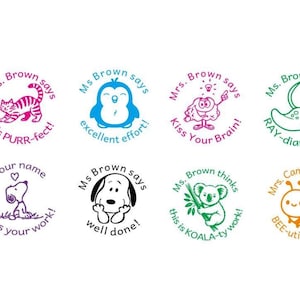 May include: Eight circular rubber stamps featuring colourful cartoon illustrations and text. Designs include a cat, penguin, brain, stingray, dog, koala, and bee with phrases like Mrs. Brown says it's PURR-fect, Ms. Brown says excellent effort, and BEE-utiful work.