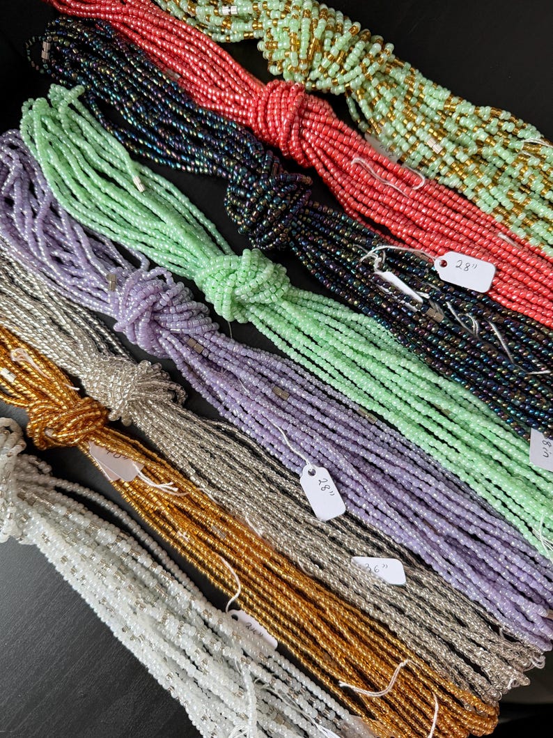 Pu&ograve; includere: Molteplici fili di piccole perline di vetro in vari colori, tra cui verde chiaro, corallo, blu scuro, lavanda, argento, oro e bianco. Ogni fascio &egrave; legato con un nodo e presenta una piccola etichetta bianca con la scritta 28 inches.