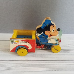 May include: A vintage wooden Mickey Mouse toy with a siren. The toy is painted red, yellow, blue, and black. The toy has a sign that reads "Mickey Mouse Safety Patrol with siren. We see, We hear. Look BOTH ways before crossing street."