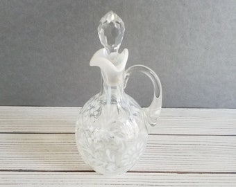 May include: A clear glass bottle with a white frosted top and a crystal stopper. The bottle has a textured surface and a handle. It is a vintage style oil and vinegar bottle.