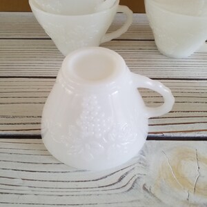 May include: A set of white milk glass cups with a floral design. The cups are stacked on top of each other and have a vintage look.
