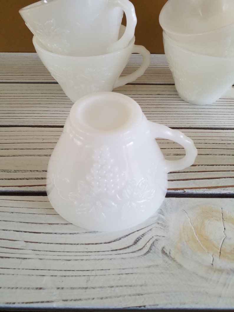May include: A set of white milk glass cups with a floral design. The cups are stacked on top of each other and have a vintage look.