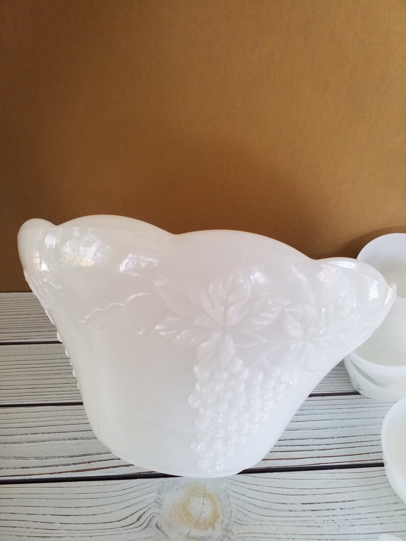 May include: White milk glass punch bowl with a grapevine design. The bowl has a scalloped edge and is in excellent condition.