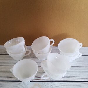May include: A set of eight white milk glass teacups with a frosted finish. The cups are stacked in pairs and have a simple, elegant design.