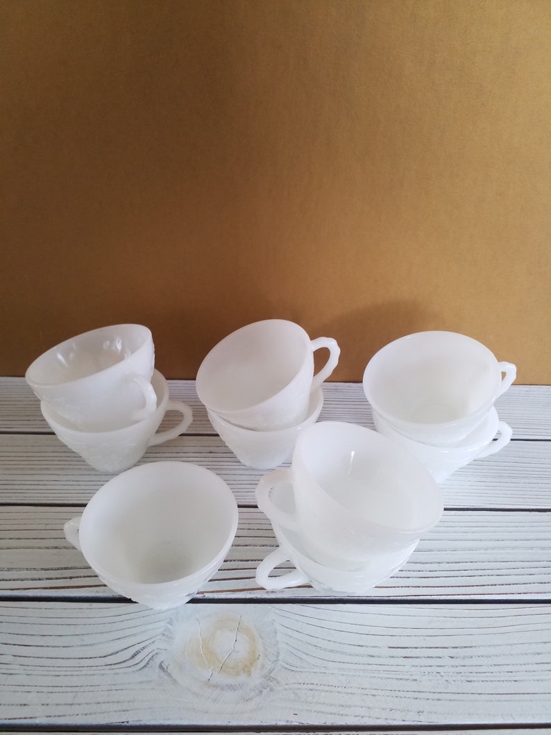 May include: A set of eight white milk glass teacups with a frosted finish. The cups are stacked in pairs and have a simple, elegant design.