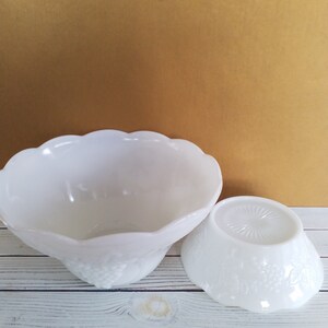 May include: Two white milk glass bowls with a grape design. The larger bowl is upside down and the smaller bowl is right side up.