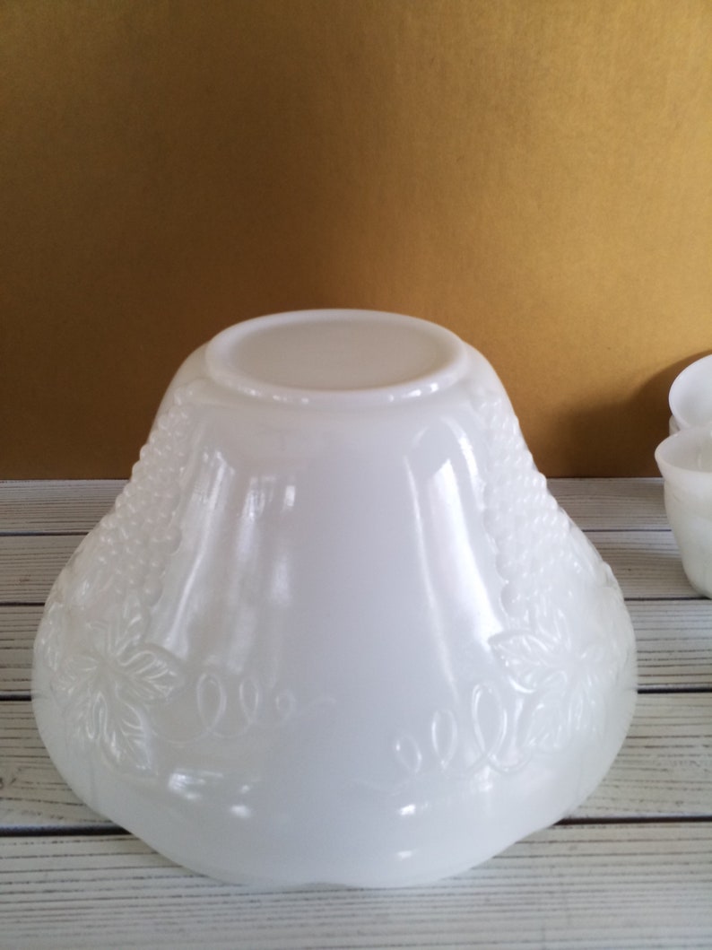 May include: White milk glass punch bowl with a grape design. The bowl is round and has a wide rim. It is made of opaque white glass and has a smooth, glossy finish.