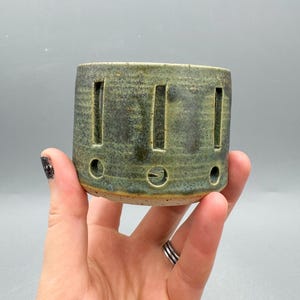 Może przedstawiać: Zestaw trzech ceramicznych kubków z nakrapianym, matowym wykończeniem. Kubki są w odcieniach kremowym, jasnoszarym i ciemnoszarym. Każdy kubek ma prosty, minimalistyczny design, idealny do kawy lub herbaty.