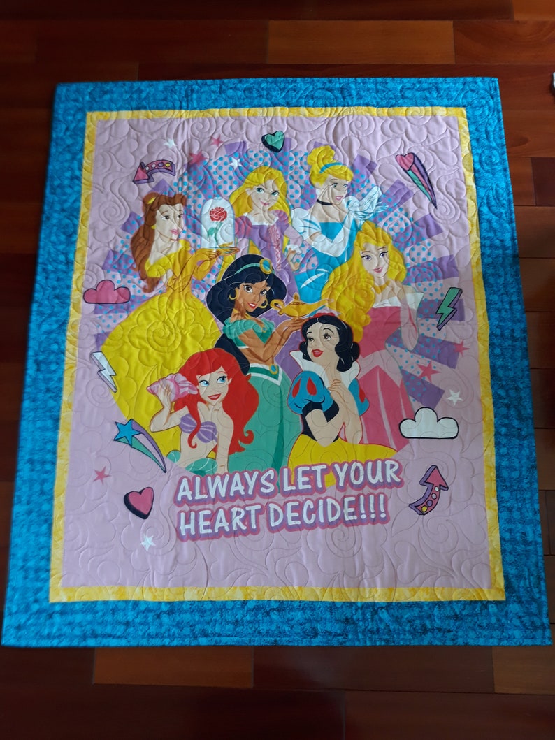 May include: A pink and blue quilted blanket with a colorful image of Disney princesses and the text "Always let your heart decide!!"
