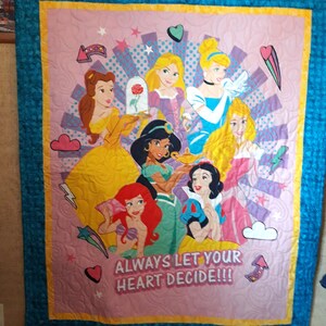 May include: A pink and purple quilt with a colorful design featuring Disney princesses. The princesses are surrounded by stars, hearts, and clouds. The text "ALWAYS LET YOUR HEART DECIDE!!!" is printed on the quilt.