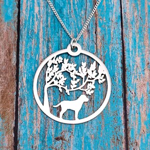Può includere: Collana d'argento con un ciondolo circolare che presenta un design ritagliato di un albero con foglie e un cane in piedi sotto l'albero.
