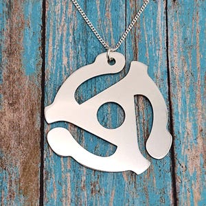 May include: A silver necklace with a pendant shaped like a vintage 45 rpm record adapter. The pendant is a cutout design, with a circular hole in the center.