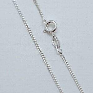 May include: A silver chain necklace with a lobster clasp. The chain is a curb style and is approximately 18 inches long.