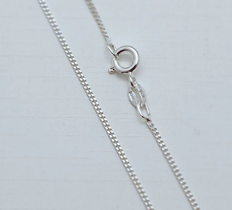 May include: A silver chain necklace with a lobster clasp. The chain is a curb style and is approximately 18 inches long.