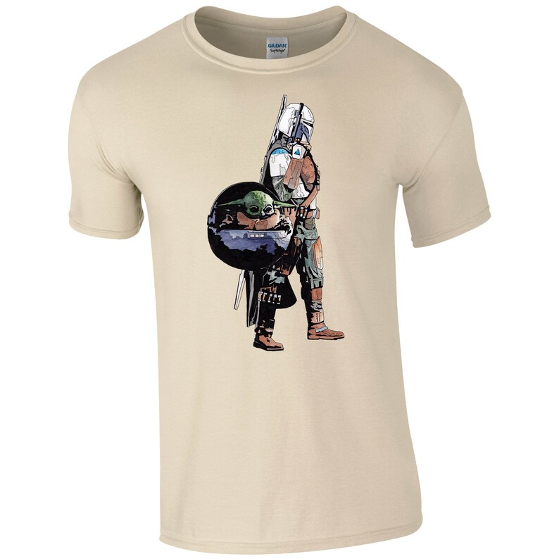 K&ouml;nnte beinhalten: Ein beiges T-Shirt mit einem grafischen Aufdruck eines Mandalorianer-Charakters aus Star Wars, der ein kleines gr&uuml;nes au&szlig;erirdisches Wesen h&auml;lt.