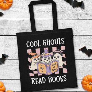 May include: Black tote bag with the text "COOL GHOULS READ BOOKS" and a graphic of three cartoon ghosts reading a book. The background includes pumpkins and paper bats, perfect for Halloween.