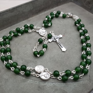 May include: A green jade rosary with silver beads and a silver crucifix. The rosary has two silver medallions with religious symbols.