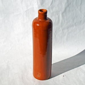 Könnte beinhalten: Eine hohe, braune Keramikflasche mit abgerundetem Oberteil und leicht ausgestelltem Boden. Die Flasche hat eine glatte, glänzende Oberfläche und ist leer.