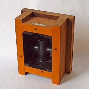 以下が含まれることがあります： 黒い金属製のインサートが付いた木製の型。型はオレンジ色に塗られており、上部に「100014」という文字が書かれた金属製のタグが付いています。