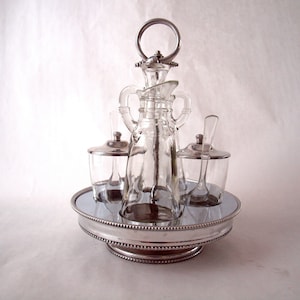 May include: A silver and glass condiment set with a central bottle and two smaller containers. The set has a mirrored base and a beaded rim.