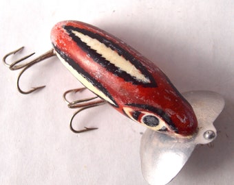 May include: A red, black, and white painted wooden fishing lure with a silver metal propeller. The lure has a black eye and a white stripe.
