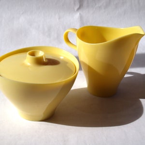 May include: A yellow ceramic creamer and sugar bowl set. The creamer has a handle and a rounded spout. The sugar bowl has a lid.