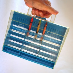 May include: A blue plastic case with a handle, labeled "72 Crayola Crayons". Three crayons are visible: red, yellow, and green.