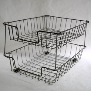 May include: A two-tiered stackable wire basket organizer made of dark gray metal. The unit features an open grid design with rectangular frames and a U-shaped cutout on the front of each basket for easy access to stored items or documents.