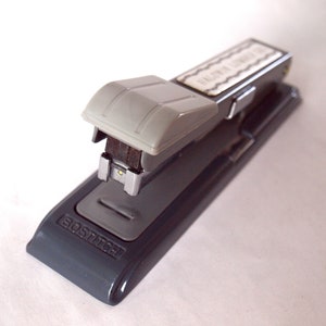 May include: A gray metal stapler with a silver top and a black handle. The stapler is labeled "BOStitch" on the bottom.