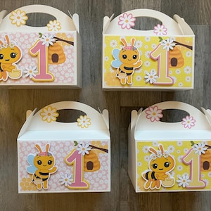 Peut inclure: Quatre boîtes blanches à pignon décorées sur le thème des abeilles et des marguerites. Chaque boîte présente une abeille de dessin animé, le chiffre 1 et un nid d'abeilles. Les boîtes ont une poignée et sont décorées de motifs floraux.