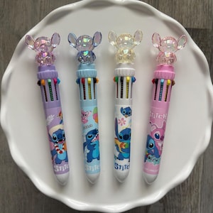 Op de afbeelding: Vier multi-gekleurde pennen met een cartoon karakter ontwerp. Elke pen heeft een verschillend gekleurde schacht, met een bijpassende topper. De pennen zijn gerangschikt op een wit, geschulpte bord. De pennen hebben het woord "Stitch" erop gedrukt.