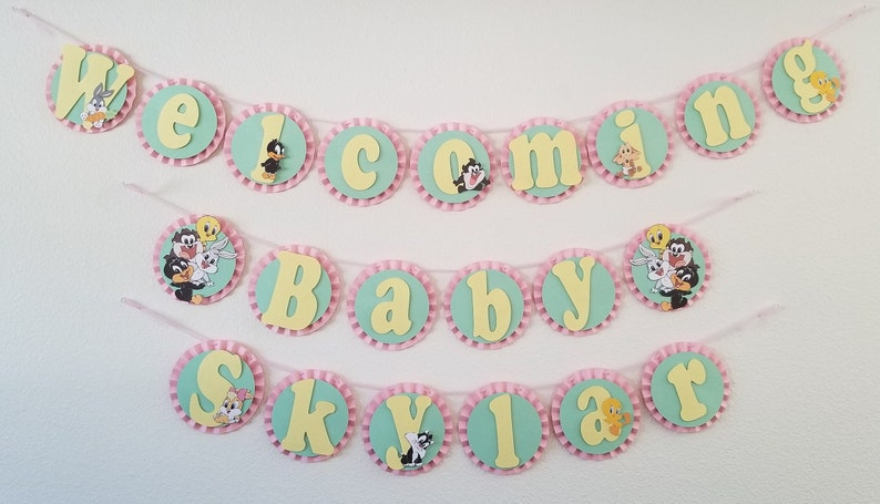 May include: A baby shower banner with a green and yellow color scheme. The banner says "Welcome Baby Skylar" and features cartoon characters from the Looney Tunes.