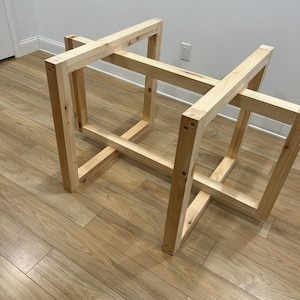 May include: A wooden table frame constructed from light-colored lumber. The frame is rectangular with intersecting horizontal and vertical supports. The table frame is unfinished and ready for assembly or customization.