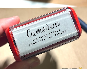 May include: A red and clear self-inking address stamp with the name "Cameron" in a script font. The address includes "123 First Street, Your City, BC V4N6N4". The stamp is from Forest Fox Press.