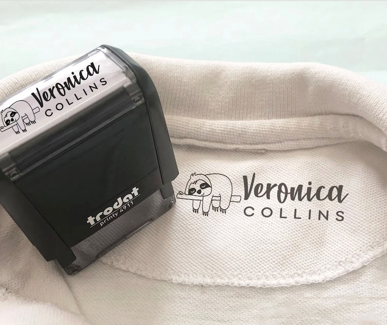 Peut inclure: Un polo blanc avec un graphique de paresseux noir et blanc et le texte "Veronica Collins" imprim&eacute; sur le col.