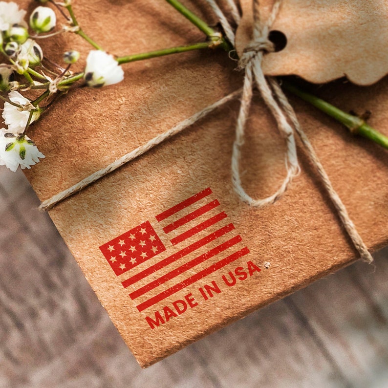 Pu&ograve; includere: Un pacco di carta marrone legato con uno spago e un timbro di bandiera americana rosso, bianco e blu che recita "MADE IN USA".