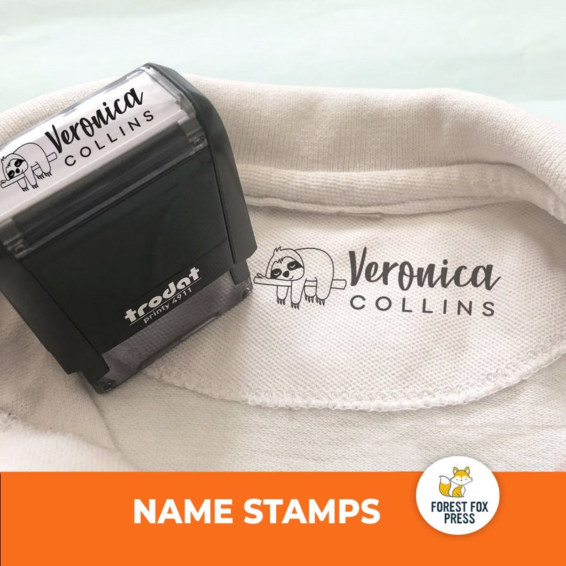 Peut inclure: Un polo blanc avec un graphique de paresseux noir et blanc et le texte "Veronica Collins" imprim&eacute; sur le devant. Un tampon auto-encreur noir avec le m&ecirc;me graphique et le m&ecirc;me texte est pr&eacute;sent&eacute; &agrave; c&ocirc;t&eacute; du polo. Le tampon est &eacute;tiquet&eacute; "trodat printy 4911".