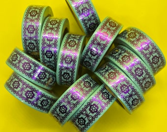 May include: A collection of green washi tape rolls with a black and iridescent floral pattern. The tape is arranged in a circle with the ends of the rolls overlapping.