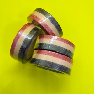 May include: Three rolls of patterned washi tape. The tape is brown with black and red stripes and white polka dots.