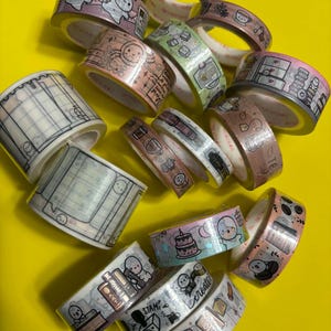 May include: A selection of washi tape rolls with diverse designs. The tapes showcase illustrations of charming characters, food, and stationery. The colour palette includes pink, blue, green, and brown. The tape rolls are displayed on a bright yellow surface.