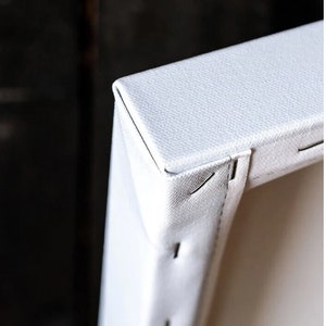 May include: Close-up of a white canvas print stretched over a wooden frame. The canvas is stapled to the back of the frame, and the staples are visible.