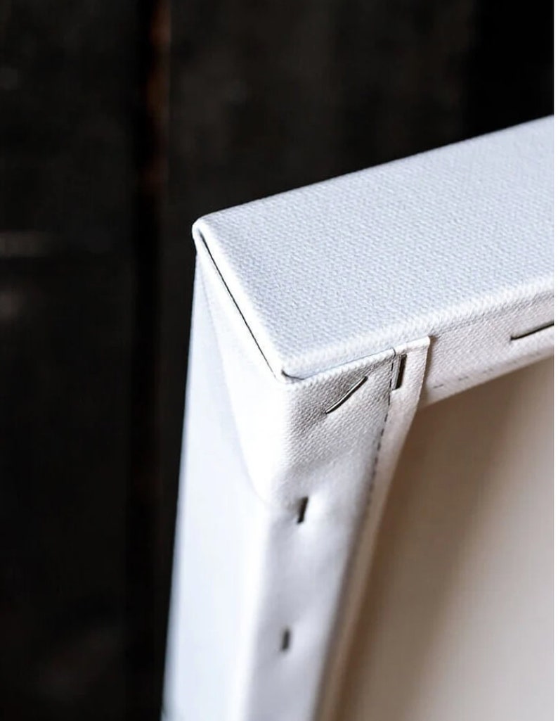 May include: Close-up of a white canvas print stretched over a wooden frame. The canvas is stapled to the back of the frame, and the staples are visible.