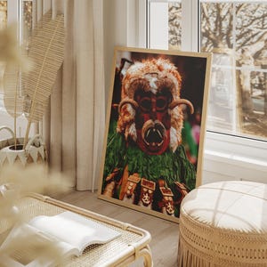 May include: A framed print of a colourful, detailed mask with a furry, brown and red design. The mask has a large, open mouth with sharp teeth and horns. The mask is set against a green and brown background.