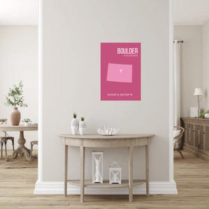 Könnte beinhalten: Ein gerahmtes rosa Poster mit dem Wort "BOULDER" und dem Umriss von Colorado in einem helleren Rosa. Das Poster enthält auch die Koordinaten 40.0150° N, 105.2705° W. Das Poster hängt an einer weißen Wand.