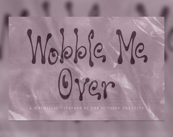 May include: A digital graphic display featuring the dark purple text Wobble Me Over in a stylized, wavy font. Below this, smaller white text reads A WHIMSICAL TYPEFACE BY THE OCTOBER CREATIVE. The entire design is set against a light purple background.