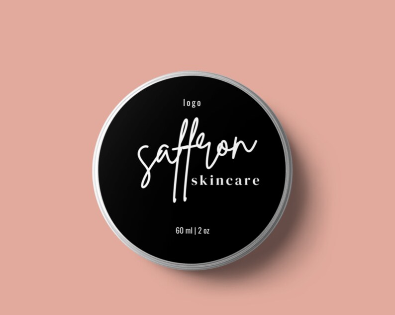 May include: A round, silver-rimmed container with a black label featuring the words "saffron skincare" in white script. The label also includes the word "logo" and the measurement "60 ml | 2 oz" on a light pink background.